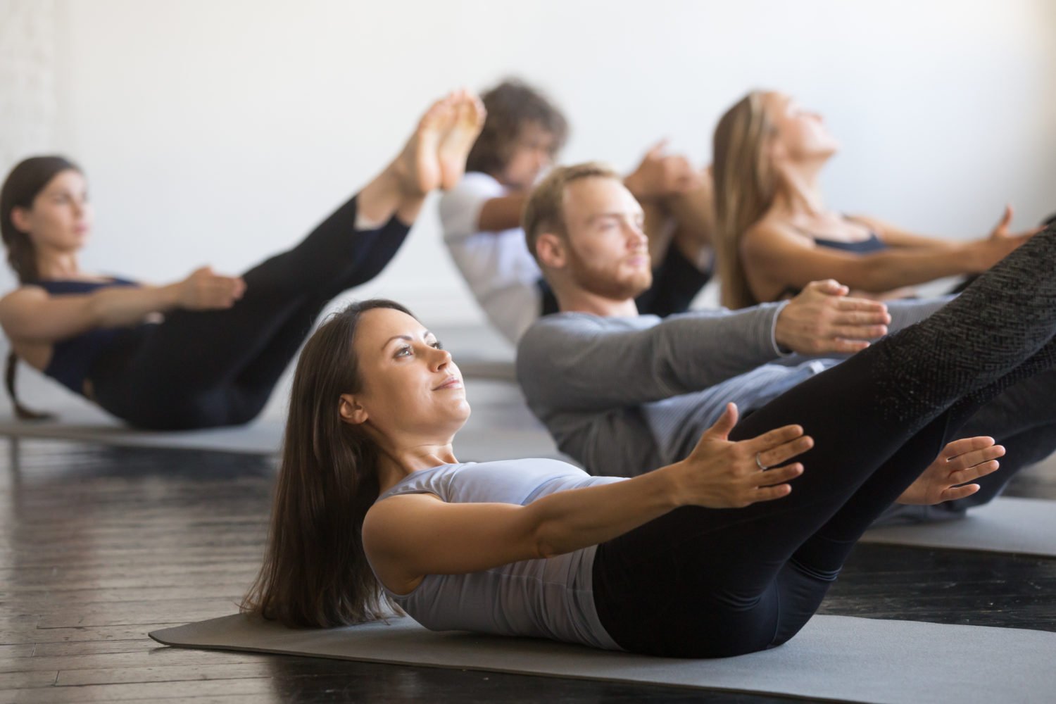 Groupe de jeunes sportifs pratiquant un cours de fitness avec un instructeur, faisant des exercices d'échauffement, pose du bateau, entraînement, étudiants s'entraînant dans un club, amis à un cours de fitness, intérieur, studio.