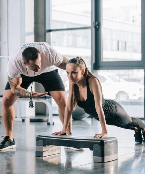 L’entraîneur personnel masculin aide une sportive à faire des pompes à la salle de sport L'entraîneur personnel masculin aide une sportive à faire des pompes à la salle de sport